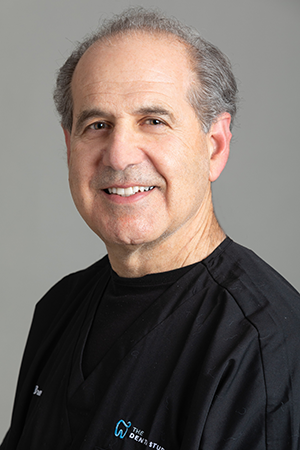 Dr. Laurence Bremmer, DMD - Summit dentist and Fellow/Master of the Academy of General Dentistry, smiling in professional attire with black medical scrubs