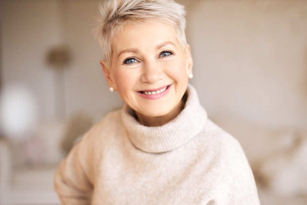 Indoor image of attractive stylish mature Caucasian female with joyful broad smile, showing perfect white teeth.